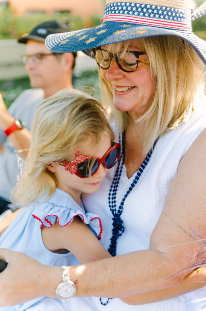 Grandmother wearing a red, white, and blue straw hat hugging her granddaughter at the Highland Park 4th of July parade.