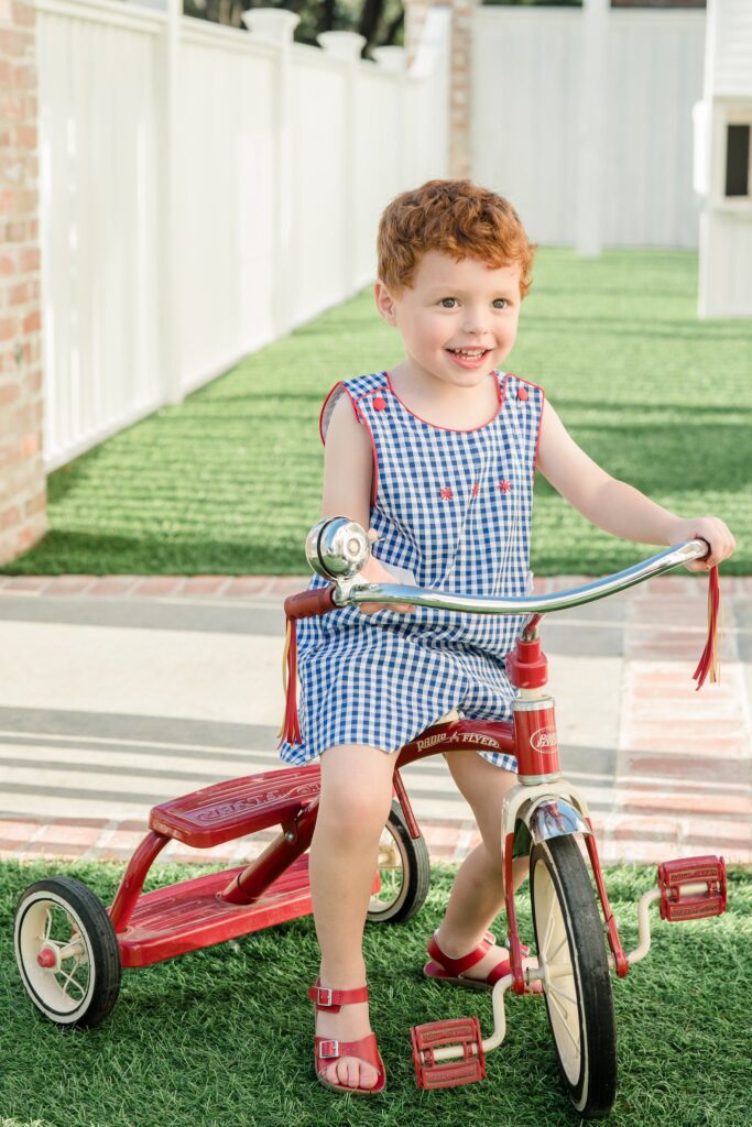 Photo of a boy riding a bike wearing a blue and white gingham outfit on the 4th of July.