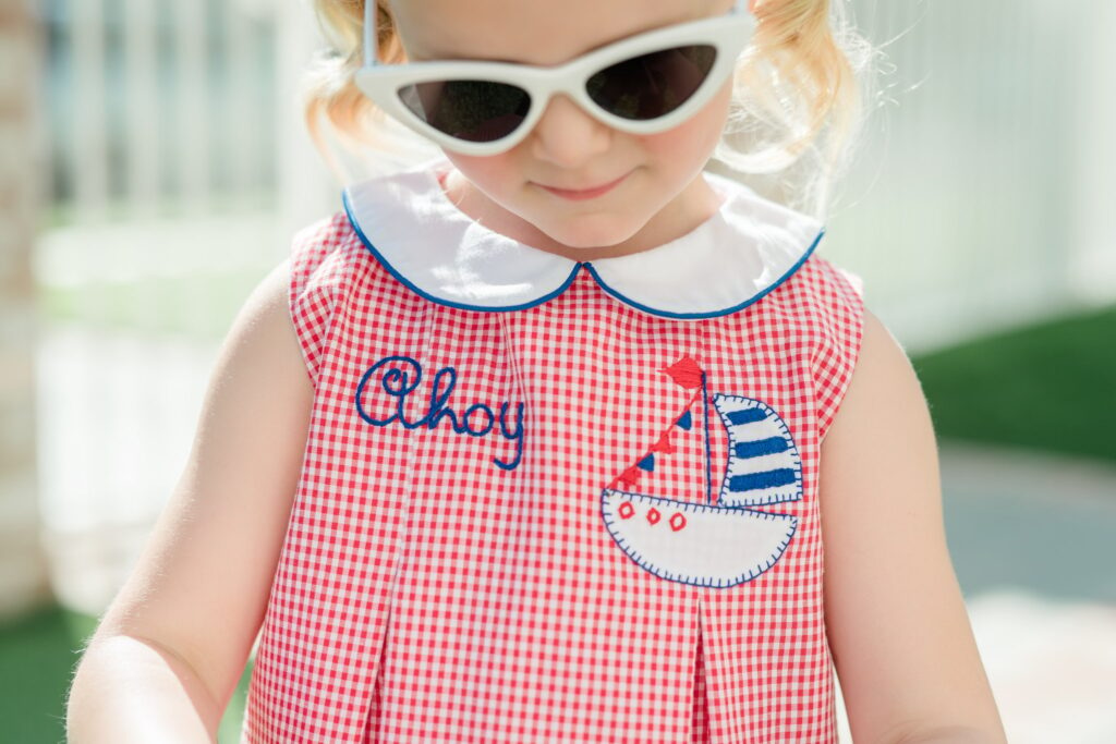Little girl wearing a gingham red patriotic dress with white sunglasses.