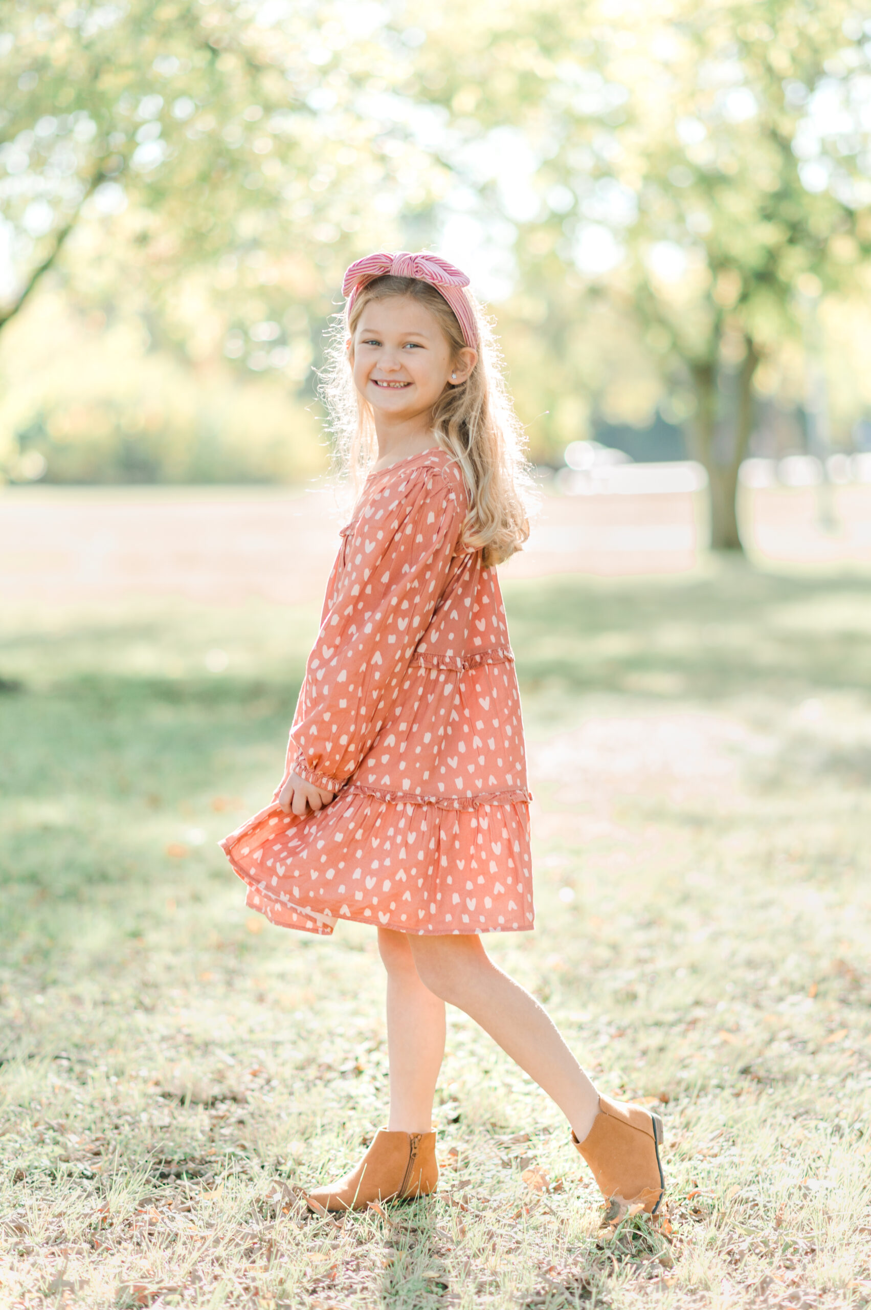Girl in a coral dress with a heart pattern twirling in a park.