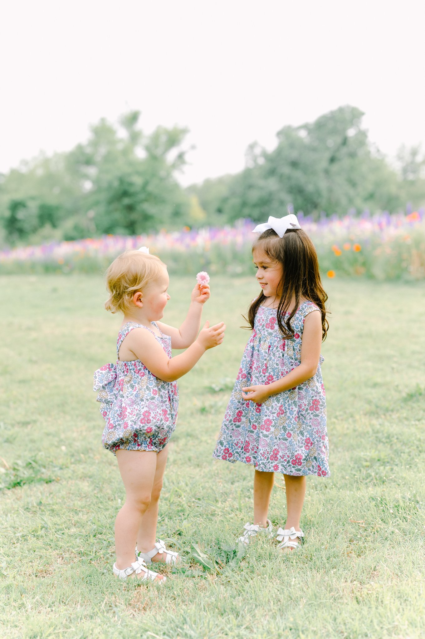 Two young girls playing in front of a field of flowers.