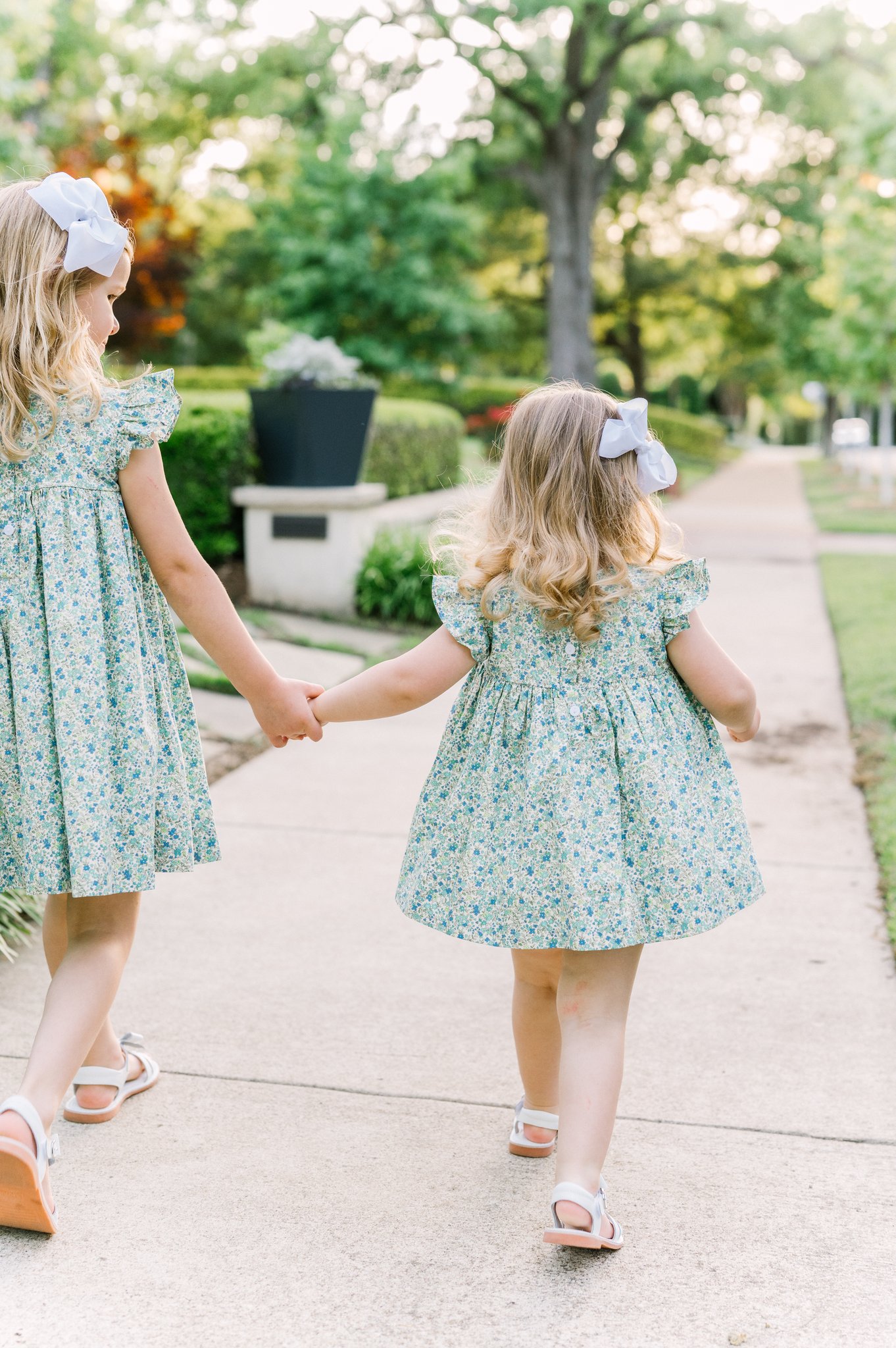Two sisters holding hands and wearing matching green dresses.