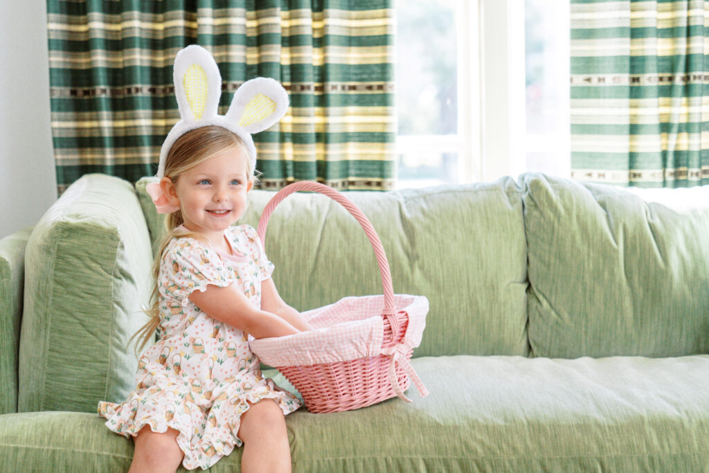 Young girl wearing bunny ears sitting on a couch in a luxury home digging through her Easter basket.